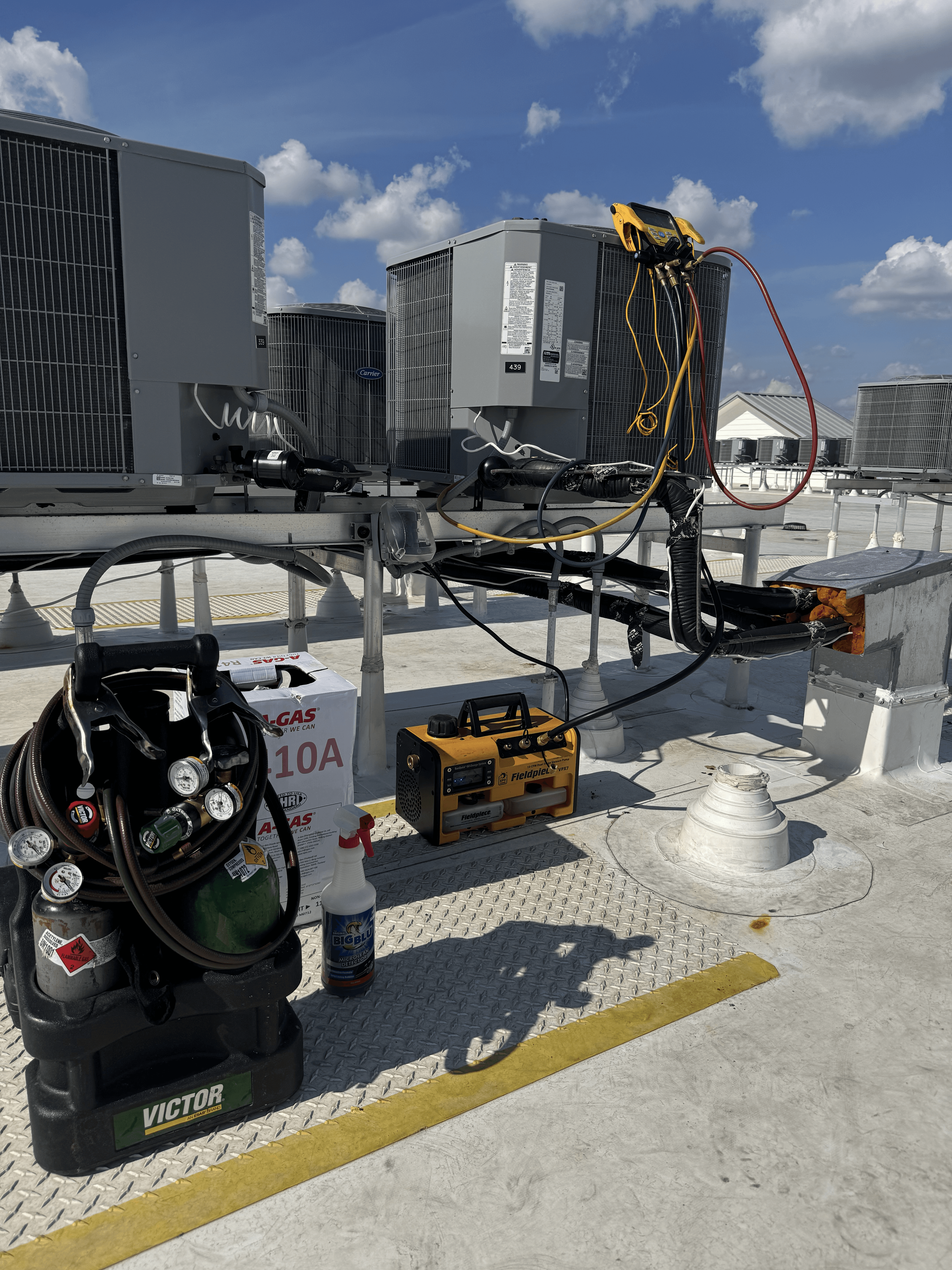 Rooftop HVAC service setup with recovery tank, vacuum pump, and service tools